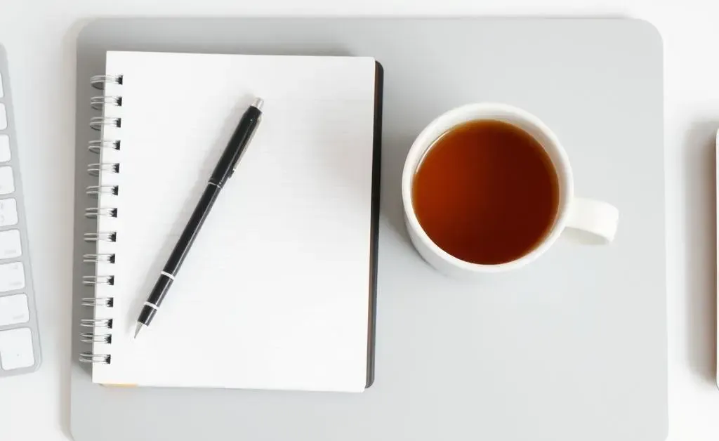 Modern minimalist desk setup with a planner, pen, and a mug of tea