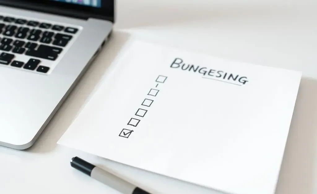 A hand-drawn checklist on a desk next to a laptop with budgeting apps open.