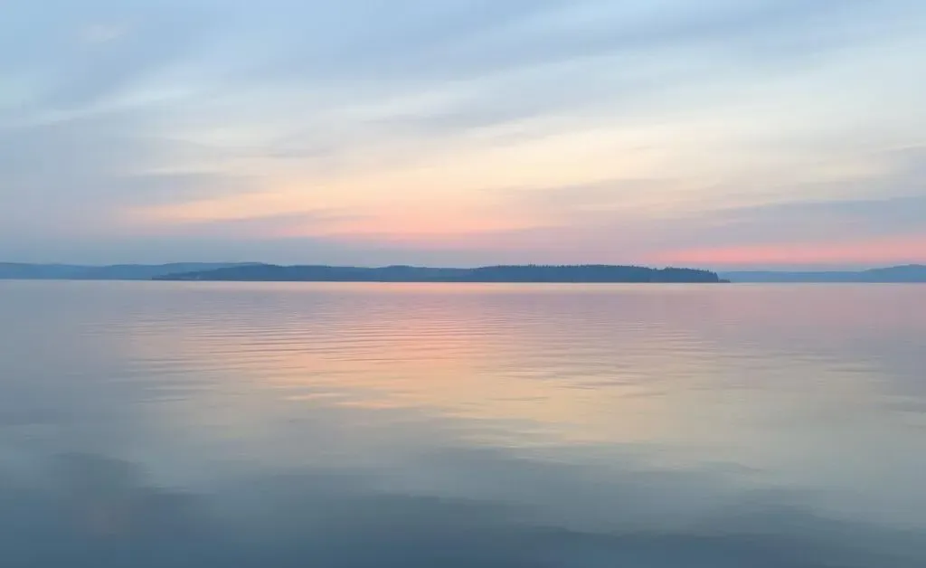 A peaceful evening view of a calm lake with soft reflections on the water.