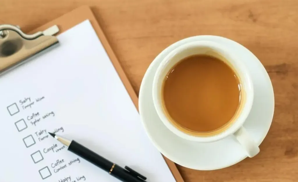 A checklist on a clipboard and a cup of coffee on a wooden table.